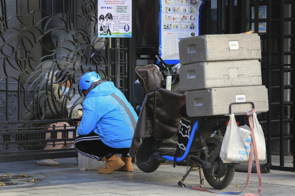 A delivery worker passes groceries to a masked woman through a closed gate at a residential block in Xi'an, a city of 13 million people under the COVID-19 lockdown, in northwest China's Shaanxi province on Monday, Jan. 10, 2022. A third Chinese city has locked down its residents because of a COVID-19 outbreak, raising the number confined to their homes in China to about 20 million people. (Chinatopix via AP)