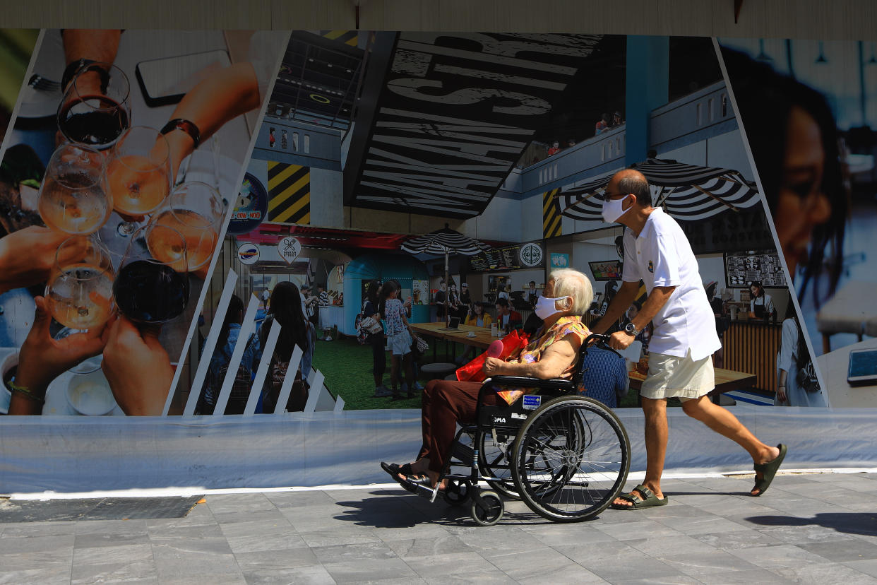 People wearing protective masks walking past an advertising billboard here on 26 May, 2020. (PHOTO: Getty Images)