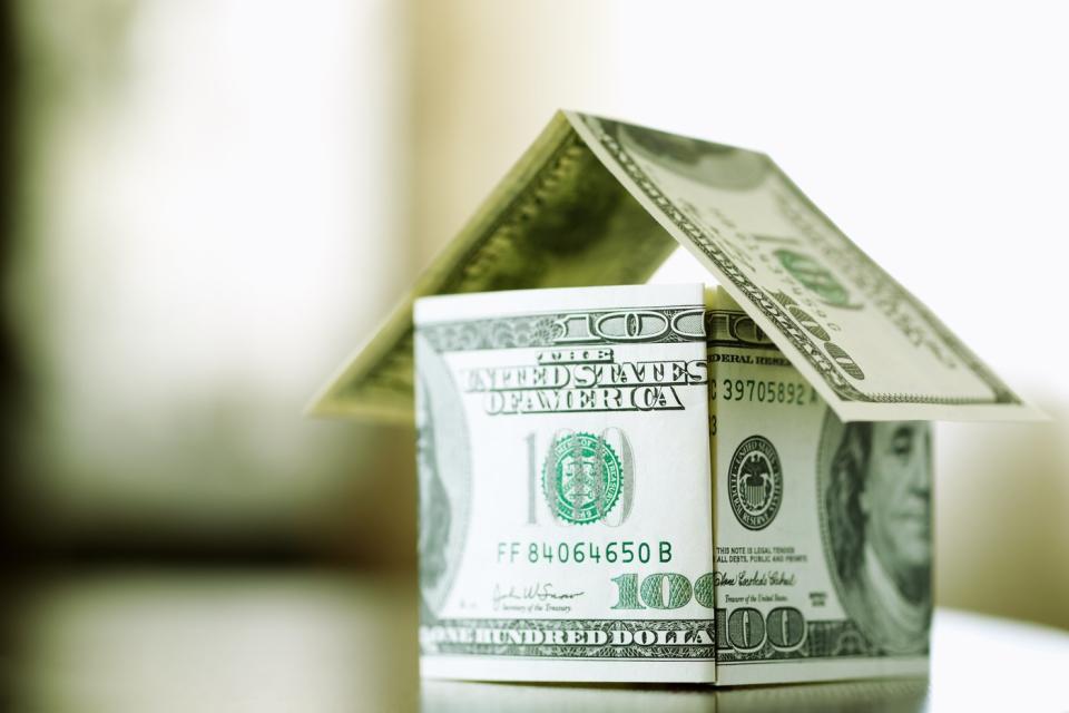 Multiple one hundred dollar bills folded into the crude shape of a house.