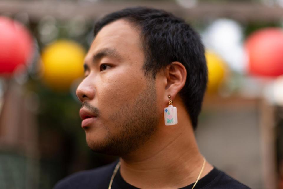 A person wears a mah-jongg-inspired earring that looks like a white tile with blue, pink and green flower engravings.