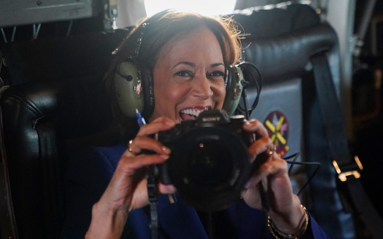 Kamala Harris reacts as she holds a photographer's camera while flying on Marine Two, on her way to O'Hare International Airport, Chicago