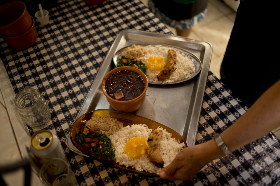 In this Sept. 15, 2012 photo, a cook prepares plates with a traditional stew called "feijoada" at the Quilombo Sacopa in Rio de Janeiro, Brazil. Quilombos are communities founded by escaped slaves or their descendents, and in Sacopa, the community is trying to save the grouping of brick houses and shacks nestled in the lush foilage of Brazil’s coastal rainforest where families have made their home for more than century but never legally owned. (AP Photo/Victor R. Caivano)