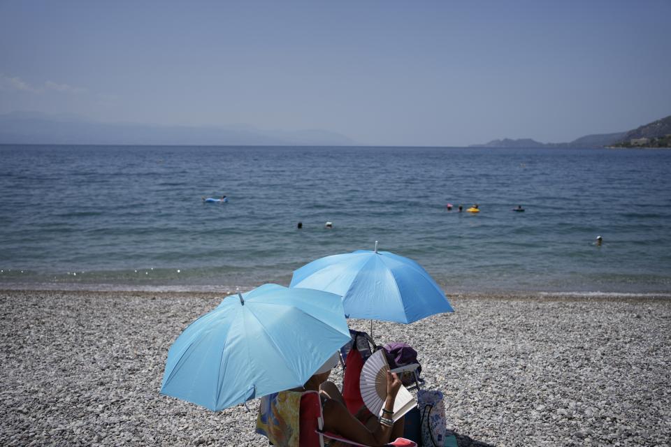 A woman using a hand fan takes cover under an umbrella at a beach in Loutraki, about 82 kilometres (51 miles) west of Athens, Greece, Thursday, July 20, 2023. Heat in Greece is expected to grow worse in the next five days, approaching 44 Celsius (111 Fahrenheit) and the country will face one more heatwave episode by the end of July, meteorologists warn. (AP Photo/Thanassis Stavrakis)