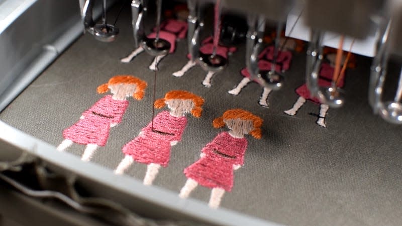 A machine embroiders three cartoon girls.