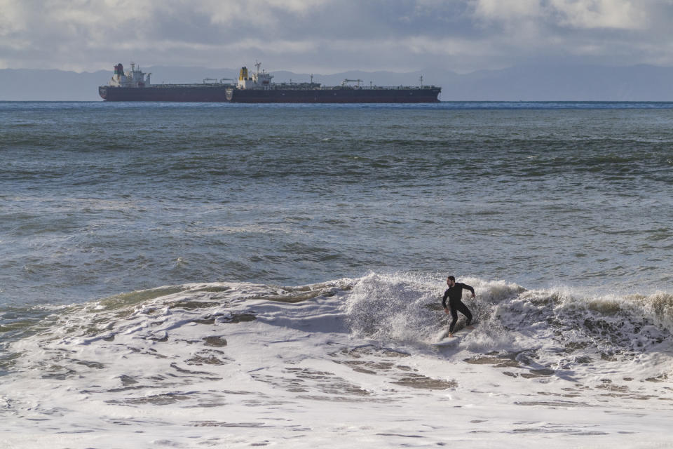 A surfer rides a large wave as shipping boats remain moored along the coast of Southern California, Saturday, Dec. 30, 2023, in Seal Beach, Calif. (AP Photo/Damian Dovarganes)