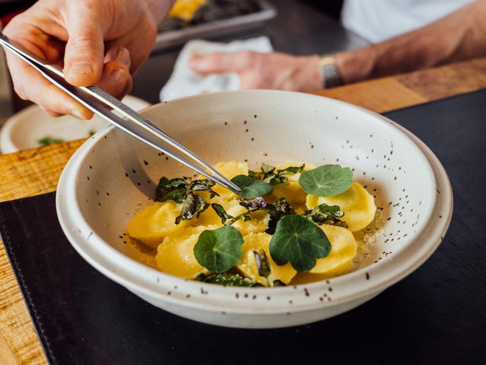 Someone plating casoncelli stuffed with mortadela, parmigiano, and pancetta.