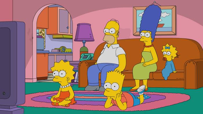 The Simpsons family sit together in the living room in front of the TV