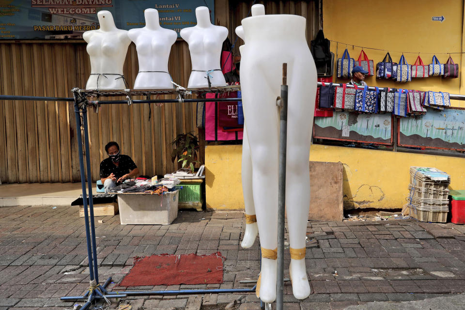 In this Thursday, April 30, 2020, photo, a street vendor waits for customers outside a shop closed due to the new coronavirus outbreak at Pasar Baru Shopping Center that is popular for its textiles products in Jakarta, Indonesia. May Day usually brings both protest rallies and celebrations rallies marking international Labor Day. This year it's a bitter reminder of how much has been lost for the millions left idle or thrown out of work due to the coronavirus pandemic. Garment workers in Asia are among the hardest hit as orders dry up and shutdowns leave factories shuttered. (AP Photo/Tatan Syuflana)