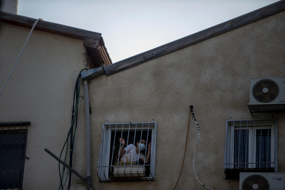 An ultra-Orthodox Jewish boy, wearing a face mask amid the coronavirus pandemic, looks out of his window in Bnei Brak, Israel Sunday, Sept. 6, 2020. The death toll from the coronavirus in Israel has surpassed 1,000, as the government on Sunday mulled steps for imposing new restrictions to quell a resurgence in infections. (AP Photo/Ariel Schalit)