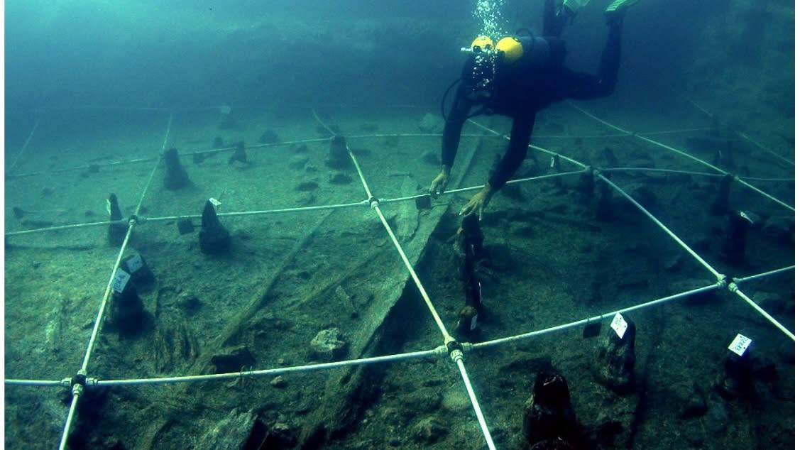  A scuba diver swimming toward a canoe underwater. 