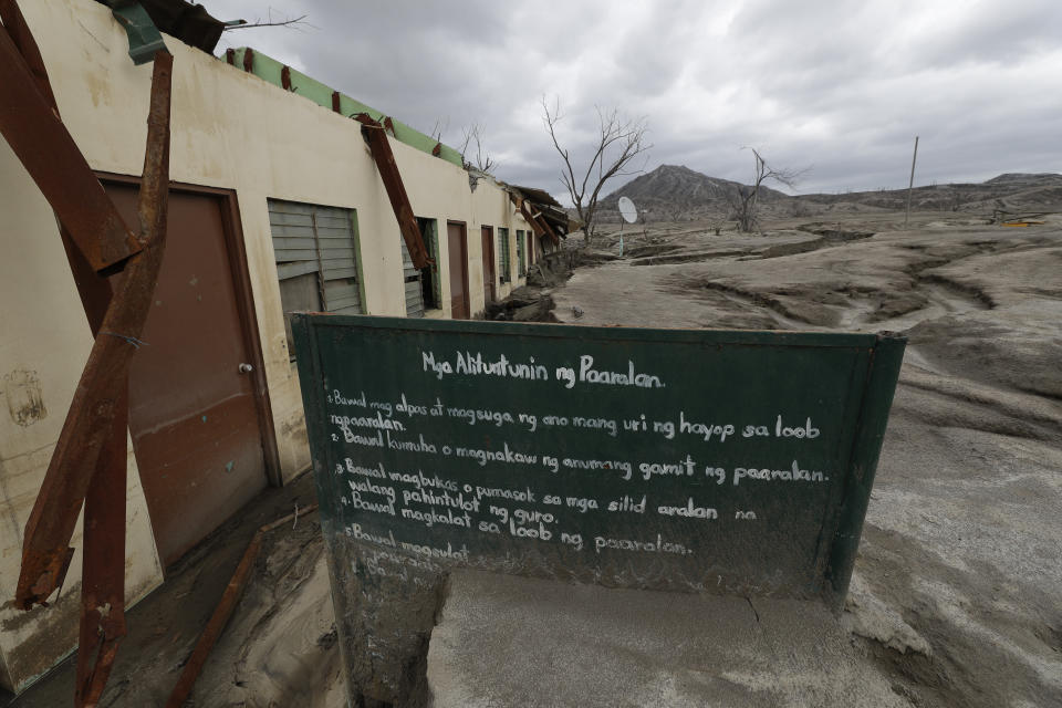 A sign stands beside the remains of the Alas-as elementary school at the Taal volcano almost a year after it erupted on Sunday, Jan. 10, 2021 in Batangas province, Philippines. A popular tourist destination just south of Manila because of its picturesque setting in the middle of a lake, Taal erupted on Jan. 12, 2020. The eruption displaced thousands of villagers living near the area and delivered an early crisis this year for one of the world's most disaster-prone nations a couple of months before the COVID-19 pandemic broke in the country. (AP Photo/Aaron Favila)