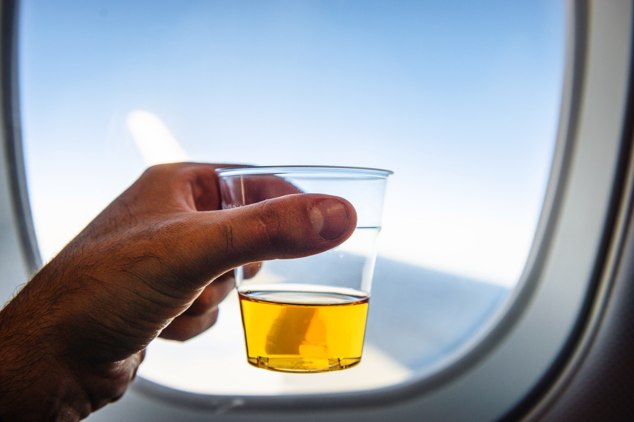 Man holding a glass of beer to the window on an airplane