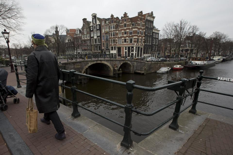 This March 20, 2013 photo shows a pedestrian passing one of the bridges in Amsterdam, Netherlands. It's not only the Rijksmuseum celebrating in 2013: Amsterdam's canals are 400 years old this year, but strolling along the waterways never gets old. The scenery includes Golden Age mansions dating to the 17th century, converted warehouses and narrow buildings that sometimes look like they're ready to topple over sideways. (AP Photo/Peter Dejong)