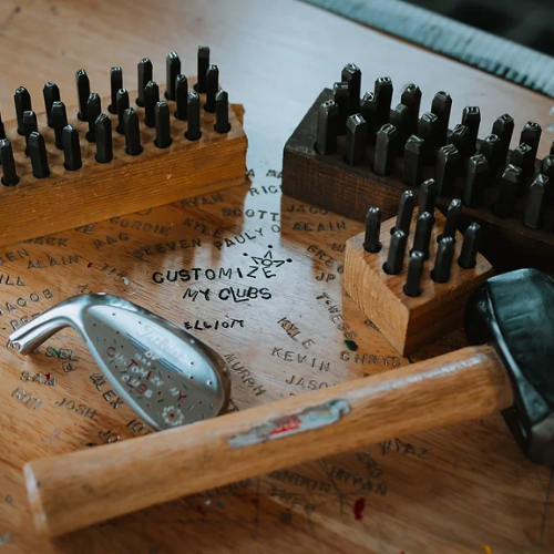 wooden hammer, golf club head on wooden table with words engraved on it