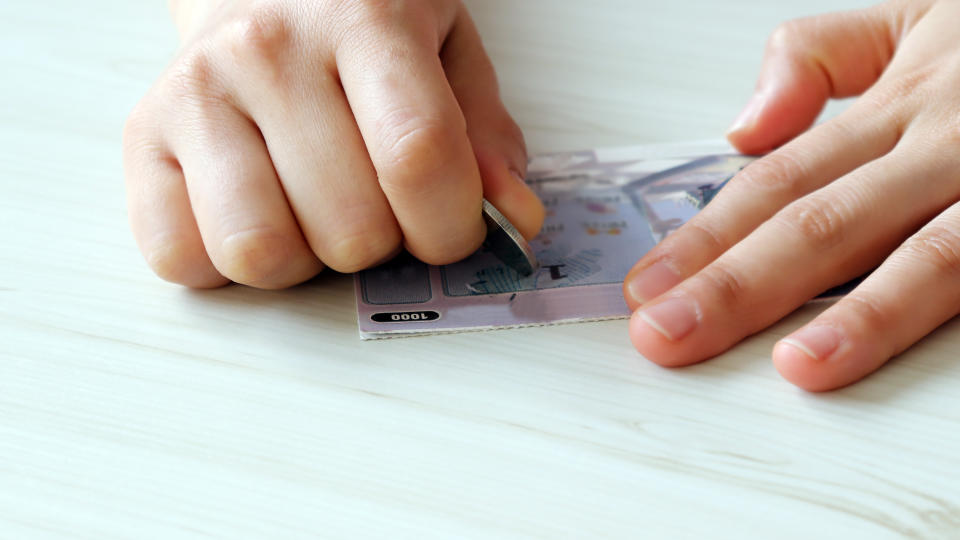 A hand scratching an instant lottery with coins.