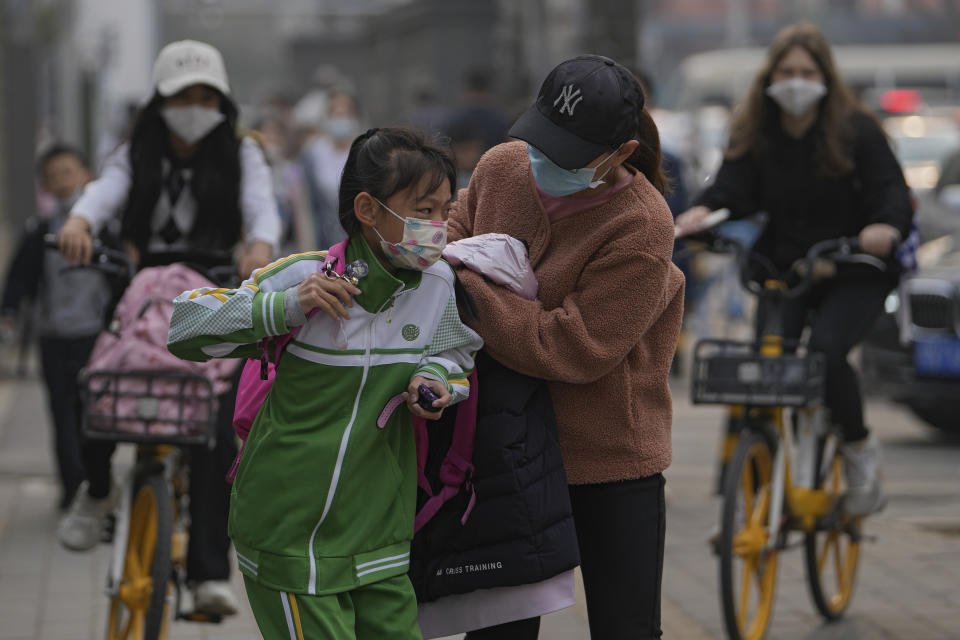 A woman wearing a face mask to help protect from the coronavirus sends a masked child to school, Monday, April 11, 2022, in Beijing. (AP Photo/Andy Wong)