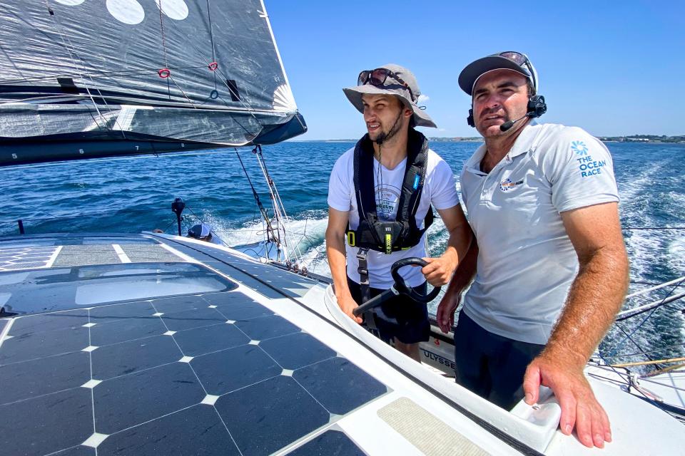 Newport Daily News reporter Zane Wolfang, left, takes the helm of the 11th Hour Racing IMOCA 60 on Narragansett Bay as skipper Charlie Enright looks on during a sail on July 22, 2022.