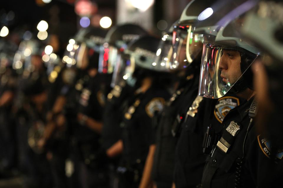 A row of police are seen wearing face shields and riot gear.