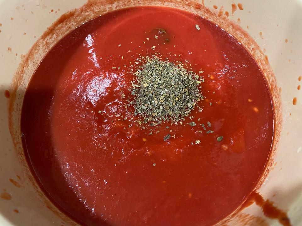 herbs being added to a 48 hour marinara sauce