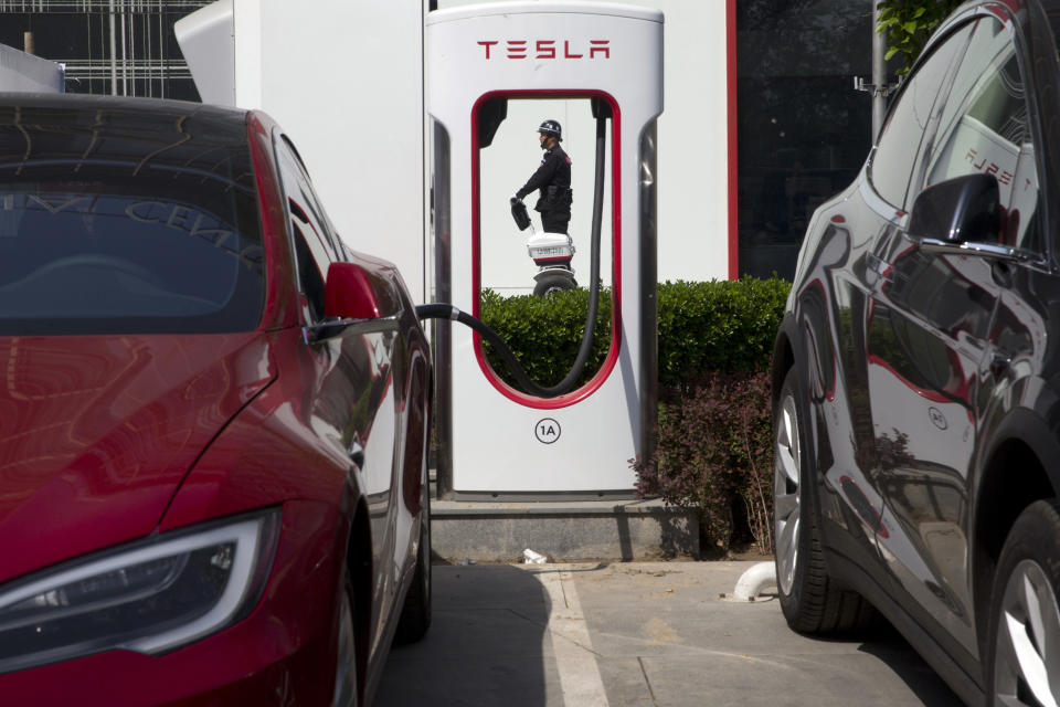 FILE - In this April 14, 2017, file photo, a security guard moves past Tesla electric vehicle charging station in Beijing. More than 200 manufacturers, including Tesla, Volkswagen, BMW, Daimler, Ford, General Motors, Nissan, Mitsubishi and U.S.-listed electric vehicle start-up NIO, transmit position information and dozens of other data points to government-backed monitoring centers, The Associated Press has found. Generally, it happens without car owners' knowledge. (AP Photo/Ng Han Guan, File)