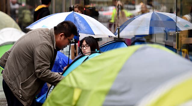 Customers shelter from the rain as they queue outside of the Apple Store in Sydney. Source: AAP