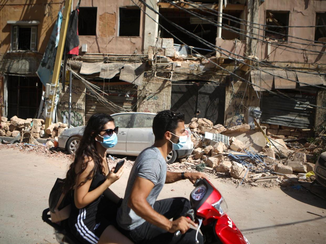 A Lebanese couple drive past the debris of a building following an explosion at Beirut's port: PATRICK BAZ/AFP via Getty Images
