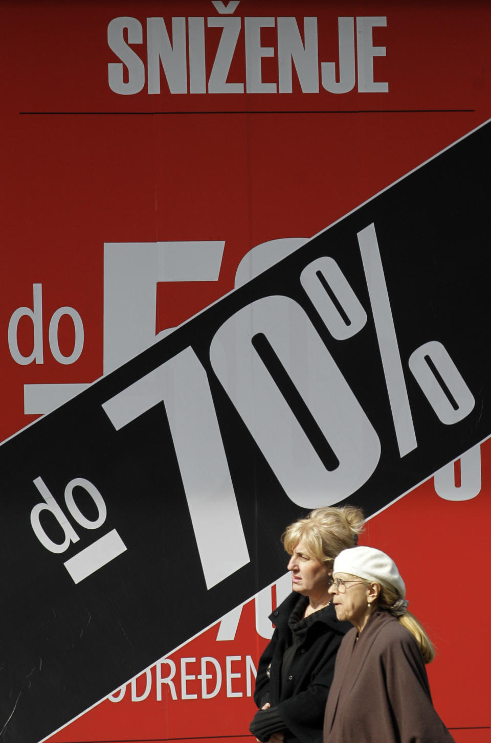 Two women pass billboard advertising an 70 percent discount on winter collection at a shop in downtown Belgrade, Serbia, Monday, March 19, 2012. Winter sales have extended well into March in Serbia and other countries in the region because of the economic crisis and a long and cold winter. (AP Photo/Darko Vojinovic)