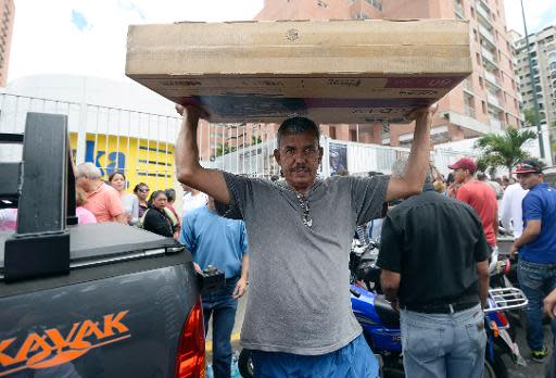 Un hombre lleva una caja con una tv de pantalla LCD comprada en la tienda Daka, intervenida por el gobierno venezolano para que bajen los precios, en Caracas, el 9 de noviembre de 2013. (AFP | Juan Barreto)