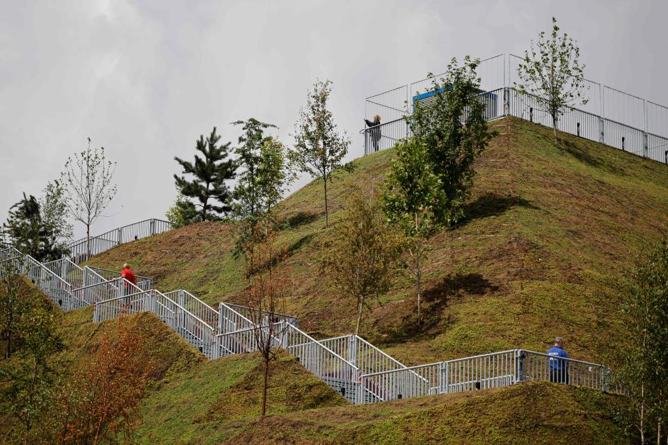 A visitor ascends the Marble Arch Mound, a new temporary attraction, as another stands on the viewing platform at the top, next to Marble Arch in central London on July 28, 2021. - A temporary tourist attraction at one end of London's busy Oxford Street has been forced to offer refunds to visitors amid widespread disappointment and derision of the grass-clad viewing platform. The 25-metre (82 feet) Marble Arch Mound had been envisaged as a draw for tourists who have typically stayed away from central London during the pandemic but only one day after opening, the local Westminster Council on Tuesday admitted it is 