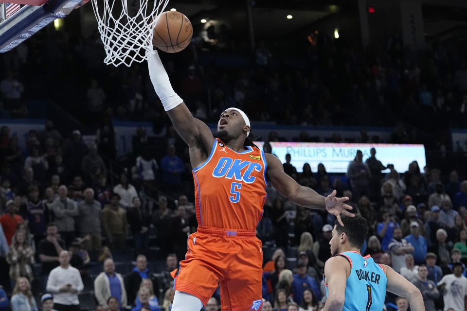 Oklahoma City Thunder guard Luguentz Dort (5) goes to the basket past Phoenix Suns guard Devin Booker (1) in the first half of an NBA basketball game Sunday, March 19, 2023, in Oklahoma City. (AP Photo/Sue Ogrocki)