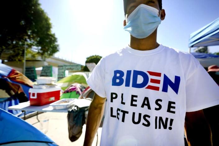 A Honduran man seeking asylum in the United States wears a shirt that reads, &quot;Biden please let us in,&quot; as he stands among tents that line an entrance to the border crossing, Monday, March 1, 2021, in Tijuana, Mexico. President Joe Biden is holding a virtual meeting with Mexican President Andr&#xe9;s Manuel L&#xf3;pez Obrador. Monday&#39;s meeting was a chance for them to discuss migration, among other issues. (AP Photo/Gregory Bull)