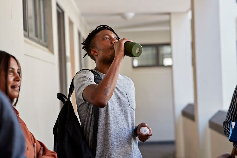 Young man drinking water from bottle while standing with female friend in corridor at university