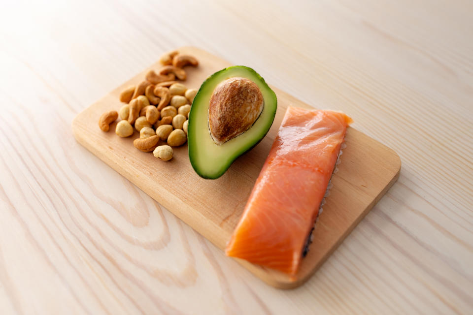 Protein diet and healthy fat concept. Salmon fillet, half of avocado and mixed nuts on cutting board on wooden kitchen table, closeup.