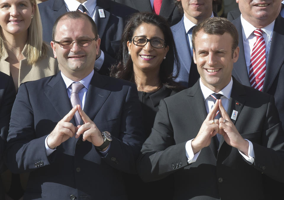 FILE - In this France, May 16, 2017 file photo, International Olympic Committee Evaluation Commission Chair Patrick Baumann, left, and new French President Emmanuel Macron make a singe representing the logo of Paris 2024 bid as they pose during a group photo at the Elysee palace in Paris. Patrick Baumann, the CEO-like secretary general of basketball’s world governing body who was seen as a potential IOC president, has died at the Youth Olympics it was announced on Sunday, Oct, 14 2018. He was 51. The International Basketball Federation says Baumann “unexpectedly succumbed to a heart attack” in Buenos Aires.(AP Photo/Michel Euler, file)