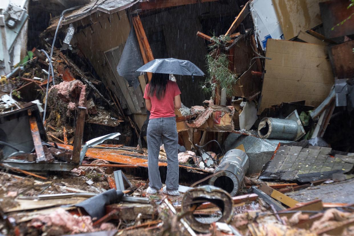 A woman stands among the wreckage of a house that was abruptly destroyed by a landslide as a historic atmospheric river storm inundates the Hollywood Hills area of Los Angeles, California, on February 6, (AFP via Getty Images)