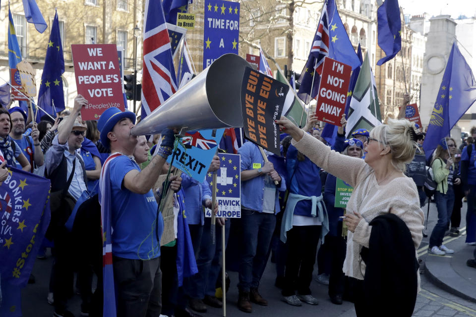 FILE - In this Wednesday, Feb. 27, 2019 file photo, a supporter of Britain's departure from the European Union, at right, holds a placard up in front of supporters of remaining in the EU, including Stop Brexit Man, Steve Bray, with his foghorn, outside Parliament in London. Five years ago, Britons voted in a referendum that was meant to bring certainty to the U.K.’s fraught relationship with its European neigbors. Voters’ decision on June 23, 2016 was narrow but clear: By 52 percent to 48 percent, they chose to leave the European Union. It took over four years to actually make the break. The former partners are still bickering, like many divorced couples, over money and trust. (AP Photo/Matt Dunham, File)