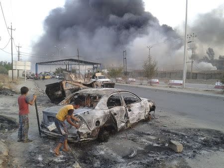 Civilian children stand next to a burnt vehicle during clashes between Iraqi security forces and al Qaeda-linked Islamic State in Iraq and the Levant (ISIL) in the northern Iraq city of Mosul, in this June 10, 2014 file photo. REUTERS/Stringer/Files