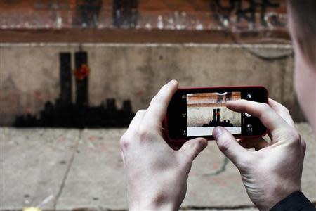 A man takes a picture of an artwork by British graffiti artist Banksy at Lower Manhattan in New York, October 15, 2013. REUTERS/Eduardo Munoz