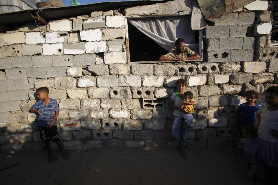 FILE - In this Tuesday, Oct. 1, 2013 file photo, Majed Alwadiya, 31, watches children of his extended family members as they play outside their family house in Gaza City in the northern Gaza Strip. The extended Alwadiya family of 38 people live in a makeshift house near a sewage plant. The makeshift house is made from scrap wood, salvaged concrete bricks and corrugated aluminum. Gaza's Hamas rulers have been hit by the worst economic crisis since seizing the territory seven years ago and face growing discontent, even among core supporters, because there's no sign of relief from a blockade enforced not only by Israel but also by a suddenly hostile Egypt. (AP Photo/Adel Hana, File)