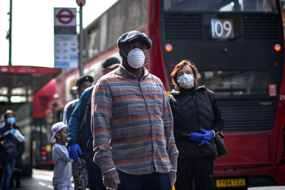 People wearing protective face masks wait in line for a supermarket in Brixton, South London, as the UK continues in lockdown to help curb the spread of the coronavirus.