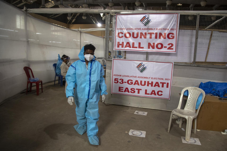 A counting agent in protective suit walks past officials during the counting of votes of Assam state assembly election in Gauhati, India, Sunday, May 2, 2021. With Indian hospitals struggling to secure a steady supply of oxygen, and more COVID-19 patients dying amid the shortages, a court in New Delhi said it would start punishing government officials for failing to deliver the life-saving items. (AP Photo/Anupam Nath)