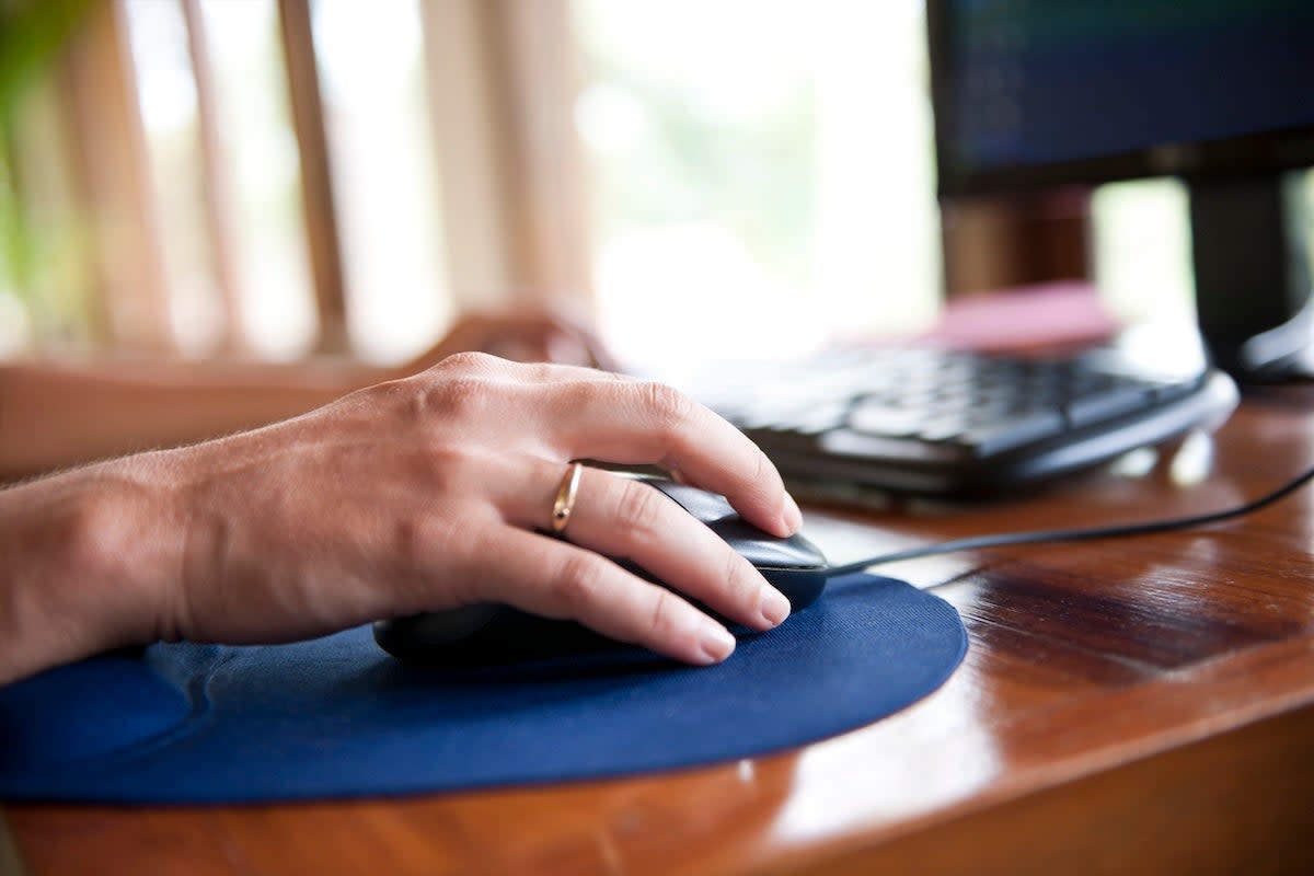 A person using a computer mouse on a mousepad on a desk in a home office.