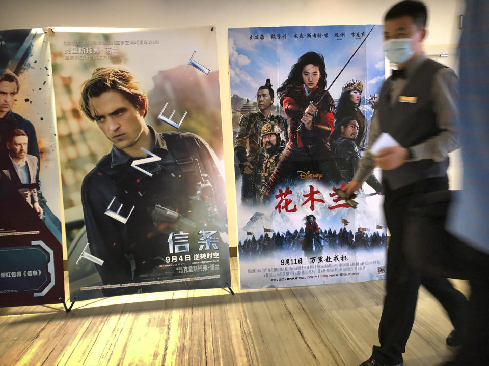 An employee wearing a face mask walks past a poster for the Disney movie "Mulan" at a movie theater in Beijing on Sept. 11, 2020. The remake of “Mulan” struck all the right chords to be a hit in the key Chinese market. Disney cast beloved actresses Liu Yifei as Mulan and removed a popular dragon sidekick in the original to cater to Chinese tastes. (AP Photo/Mark Schiefelbein)