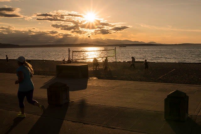 File: The sun setting on Alki Beach with views of the Olympic Mountains and downtown Seattle.