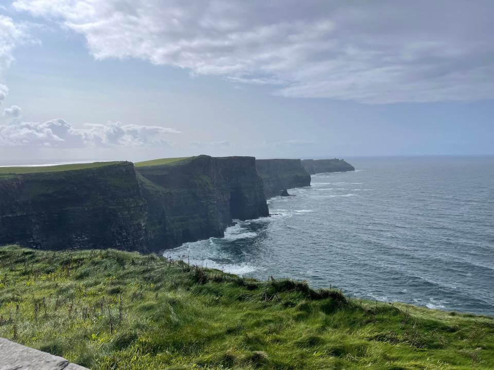 Cliffs overlooking seaside with waves crashing against rocks and clouds overhead in Ireland