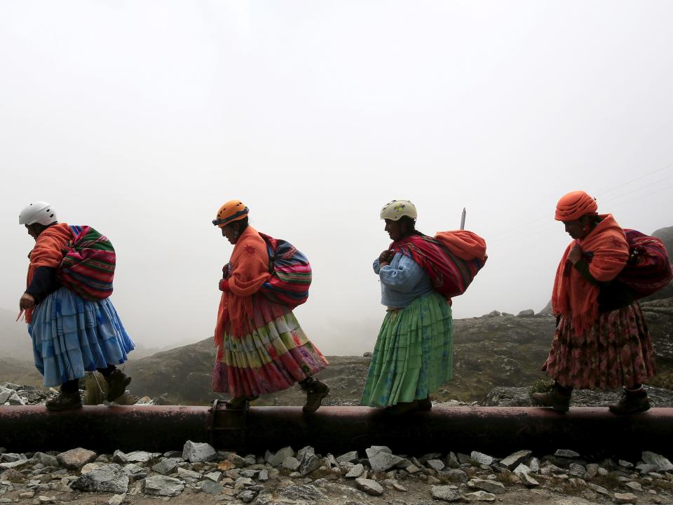 A photo of four Aymaran women walking in a single file line.