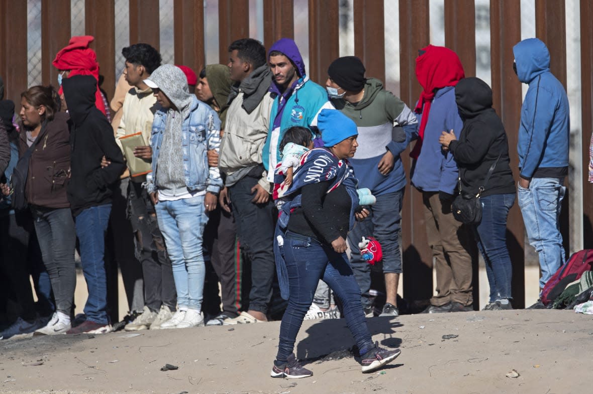 FILE – A migrant woman carries a child on her back while looking at the line of fellow migrants attempting to enter into El Paso, Texas, after crossing the Rio Grande from Ciudad Juarez, Mexico, Dec. 21, 2022. Texas and Florida are being led by tough-talking Republican governors weighing presidential runs as their state lawmakers debate especially strict legislation on border security. (AP Photo/Andres Leighton, File)