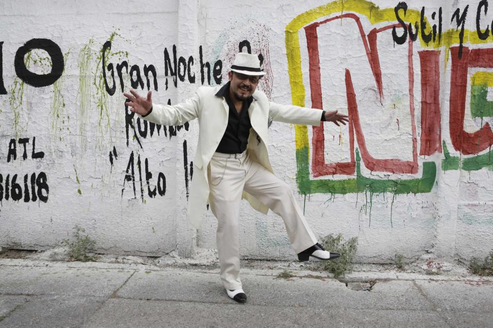 Guardarrama Tapia wears his "Pachuco" outfit while posing for a photograph next to a wall with graffiti in Mexico City