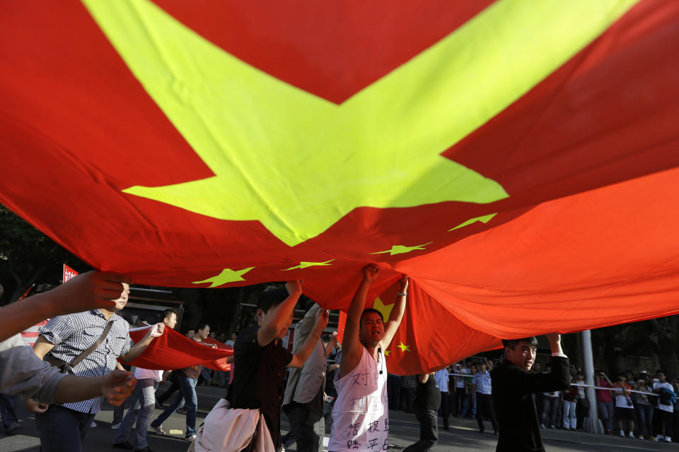 Chinese protesters march under a large national flag near the Japanese Embassy in Beijing Sunday, Sept. 16, 2012. Security personnel tightened their guard of the embassy on Sunday as crowds of Chinese continued to protest in the capital and across the country in sometimes violent demonstrations over islands claimed by both nations. (AP Photo/Ng Han Guan)