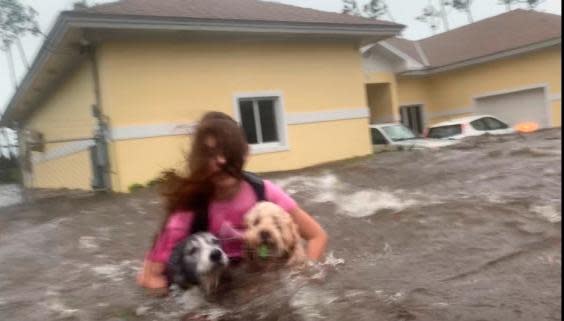 Julia Aylen wades through water carrying her dogs after her home in Freeport, Bahamas, was flooded by Hurricane Dorian (AP)